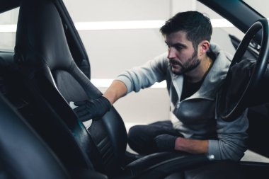 Man cleaning car interior by hand. Professional car detailing studio owner washing leather car seats with a clean rug. High quality photo