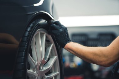 Blackening tire wheel with a sponge. Car detailing process. Closeup indoor shot. Unrecognizable male specialist during work. High quality photo
