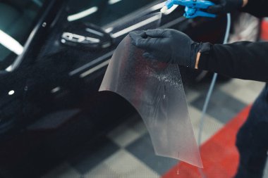 Paint protection film installation on side mirror of a black sports car. Top indoor view. Unrecognizable man. Protective gloves. High quality photo