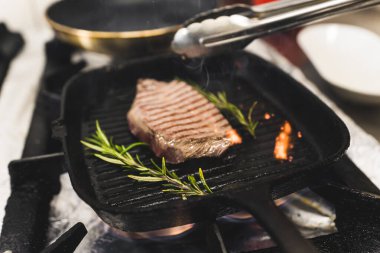 Preparing beef striploin steak with herbs on grill frying pan. Restaurant kitchen food preparation process. Horizontal indoor shot. High quality photo