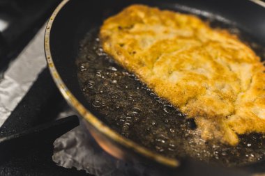 Breaded pork cutlet schabowy frying in oil in frying pan. Polish cuisine. Restaurant kitchen food preparation process. Horizontal indoor close-up shot. High quality photo