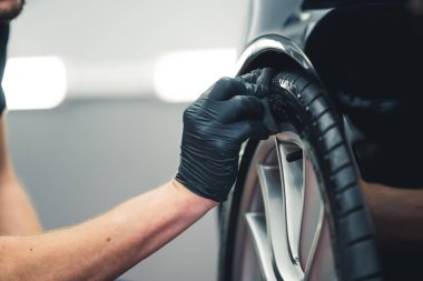 Tyre blackening process. Unrecognizable man blackening a tyre with a sponge. Professional car detailing in a garage. High quality photo