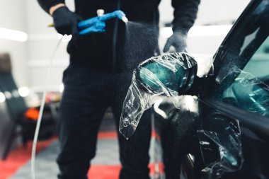 Transparent protective film applied on a black car. Unrecognizable car detailing expert spraying onto a car. Paint Protection Film. High quality photo