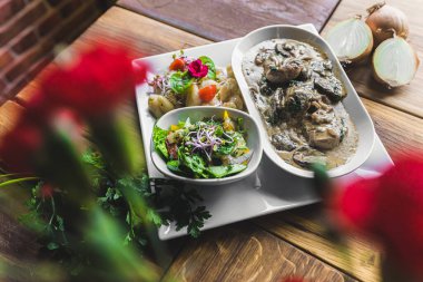 Pork fillets in bolet mushroom sauce gravy served with roasted potatoes and salad on white plate. Restaurant table. Horizontal indoor shot. High quality photo