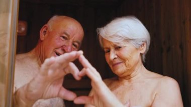 Romantic old couple making heart sign with hands looking at each other with love. High-quality 4k footage
