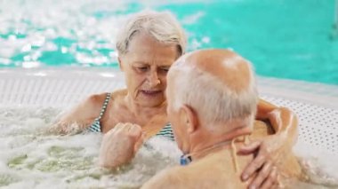 Romantic senior couple in a swimming pool talking with arms around each other. High-quality 4k footage