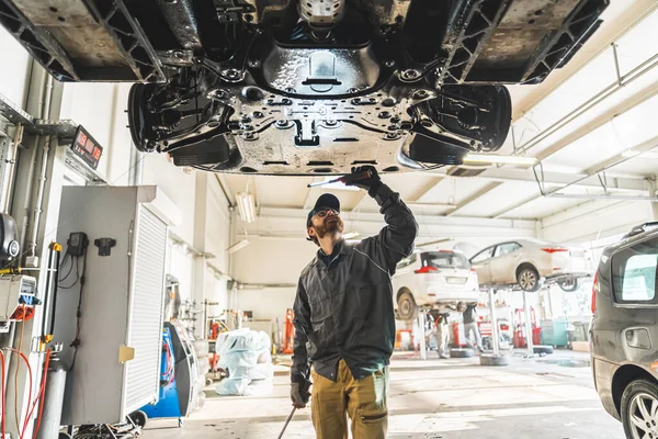 medium shot of an auto mechanic using a diagnostic tool at a car repair shop, chassis inspection. High quality photo