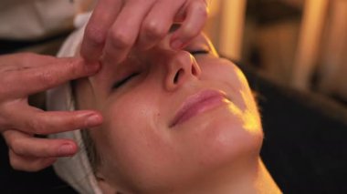 Beautician massaging her female clients forehead and eyebrows. Blurred background. High quality 4k footage