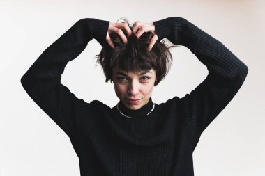 Studio portrait of confident unusual young adult woman touching ruffled hair with both hands and looking at camera. WHite background. High quality photo