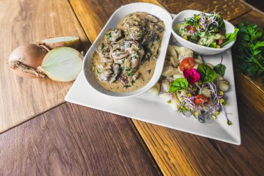 Pork fillet dish with bolet mushroom gravy sauce served with potato dumplings and fresh salad. Rustic wooden table decorated with onions and herbs. Horizontal indoor shot. High quality photo