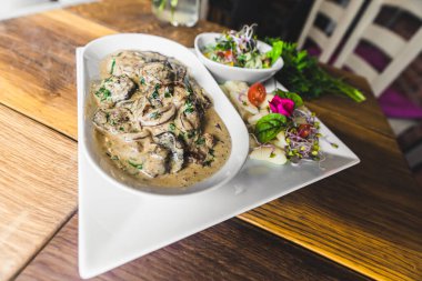Pork fillets dish with bolet mushroom gravy sauce with potato dumplings and salad served on white plate. Restaurant table. Horizontal indoor shot. High quality photo