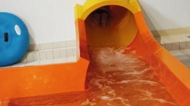 An adventurous man plunges into the pool with a splash from an orange tunnel slide. High-quality 4k footage