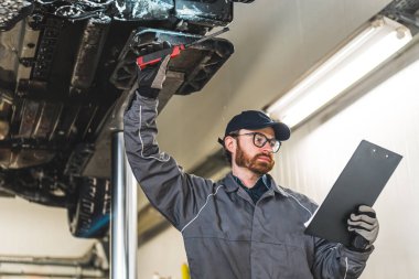 an auto serviceman looking into the papers while chassis inspection in a car workshop, medium closeup. High quality photo