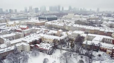 Şehrin karla kaplı çatıları ve caddelerinin arka planında şehir merkezi olan havadan çekilmiş videosu. Winter City konsepti. - Evet. Yüksek kalite 4k görüntü