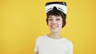 Positive VR experiences. Young female gamer looking at camera and smiling with virtual reality headset on her head. Orange background. High quality 4k footage