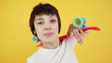 Happy young person with small skateboard on shoulders looking at camera and smiling. Medium closeup studio shot over orange background. High quality 4k footage