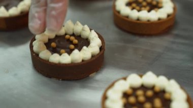 Mini tarts being decorated with golden pearls on a metal baking tray. Blurred mini tart in the foreground. High quality 4k footage
