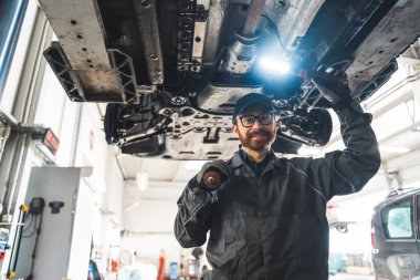 Mechanic standing under a car on a lift and holding a flashlight. High quality photo