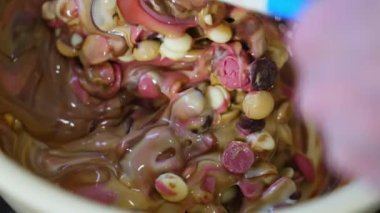 Unrecognisable chocolatier melting and mixing white pink and milk chocolate pellets in a bowl using spatula. Chocolate production. Horizontal indoor close-up video. High quality 4k footage