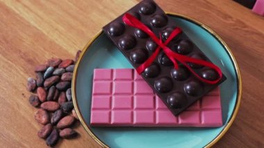 Top-down view of dark chocolate bar decorated with red ribbon on pink chocolate bar on blue and gold plate transitioning into ice cream cones. Craft premium chocolate gift set. Valentines Day