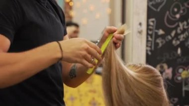 Blonde female client having her hair cut by male hairdresser in the professional hair salon. Blurred background. High quality 4k footage