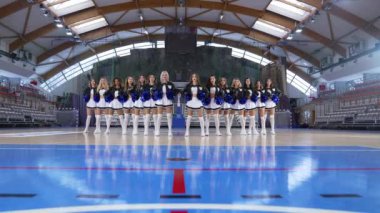 cheerleaders with black-white uniforms and blue pom-poms standing confidently in the arena. High quality 4k footage