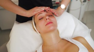 Attractive woman with eyes closed getting a gentle relaxing face massage in a beauty clinic. High quality 4k footage