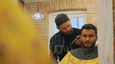 Medium shot of a male client on a hairdressers chair having his hair trimmed. Video taken in a mirror. Partially obstructed foreground. High quality 4k footage