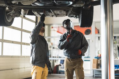Two mechnics during work. One holding a flashlight, another inspecting cars bottom. High quality photo