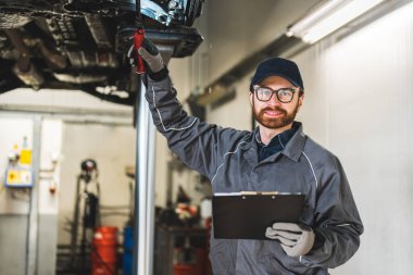 Mechanic holding a writing pad in one hand and a tool in another, and smiling at the camera. High quality photo