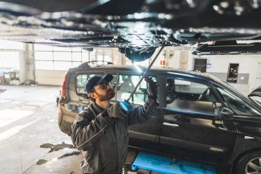 Medium high angle shot of a mechanic doing car chassis inspection. Another car in the background. High quality photo
