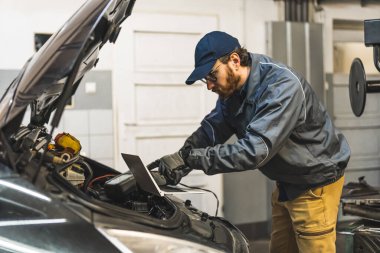 Picture of a mechanic using his computer to do a car check-up. Medium shot. High quality photo