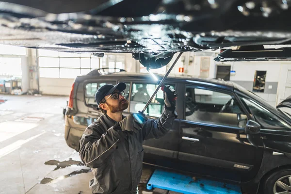 Medium high angle shot of a mechanic doing car chassis inspection. Another car in the background. High quality photo