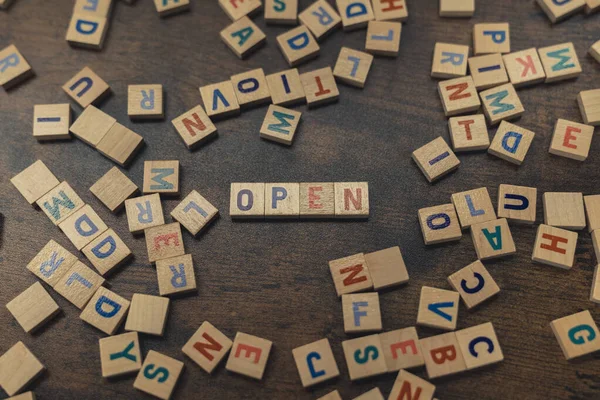 Open word spelled with Scrabble tiles on wooden table with other tiles scattered. High quality photo