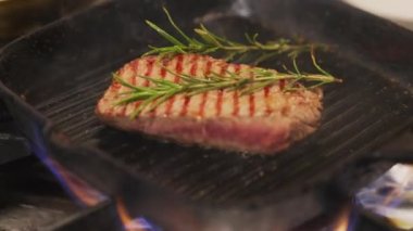 Chef adds rosemary to juicy beef steak cooking on a flaming cast iron grill pan. High-quality 4k footage
