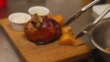 Chef adds roasted potatoes with baked pork knuckles or Golonka on a wooden board. High-quality 4k footage