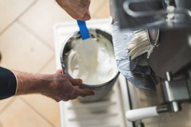 Close shot of man hands with a stirring paddle mixing ice cream from freezer in a steel container. High quality photo
