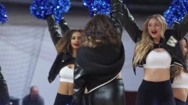 happy cheerleaders with blue pom-poms celebrating their teams score, sports concept indoors. High quality 4k footage