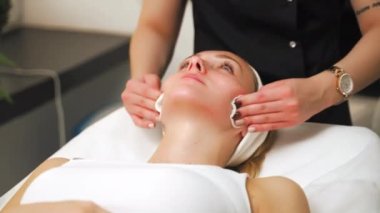 Beautician wiping womans face using cotton swabs after facial beauty treatment. High quality 4k footage