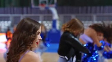 medium closeup view of a curly-haired pretty cheerleader dancing with her team in the arena. High quality 4k footage