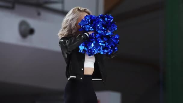 Blond Haired Confident Cheerleader Dancing Waving Blue Pom Poms Indoors — Stockvideo