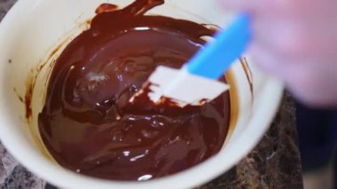 Unrecognisable chocolatier stirring melted chocolate in a bowl using spatula. Chocolate production process. Horizontal indoor close-up video. High quality 4k footage