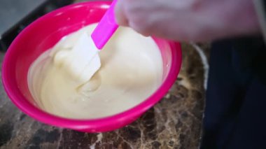 Close-up of unrecognisable chocolatier stirring melted white chocolate in red bowl using spatula. Chocolate production process. Horizontal indoor video. High quality 4k footage