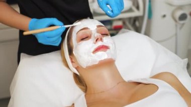 Beautician applying face peeling mask to her clients face using a brush in a spa. High quality 4k footage