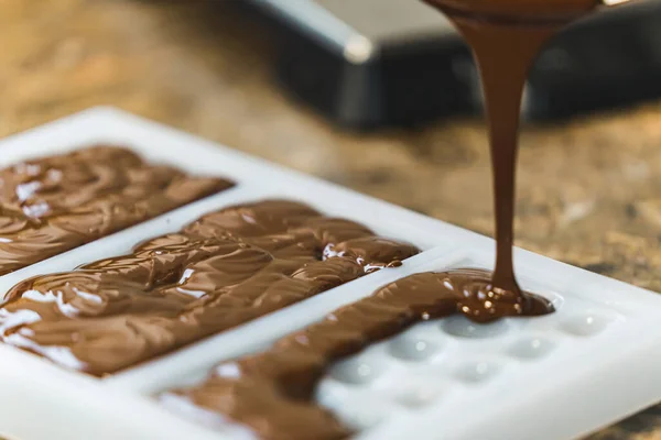 Chocolate making workshop. Milk chocolate being poured into moulds to create bars in different shapes. Closeup shot. High quality photo
