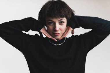 Siyah balıkçı yaka kazaklı, kısa saçlı bir kadının ellerinin arkası yanaklarında poz verirken orta boy fotoğrafı. Yüksek kalite fotoğraf