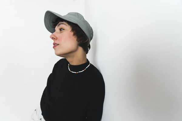Side medium shot of a woman with parted lips wearing a cap, a necklace and a black sweater. High quality photo