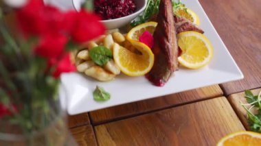 Portakal dilimleri, nane yaprakları ve patates köfteleriyle beyaz tabakta servis edilen ördek filetosu..