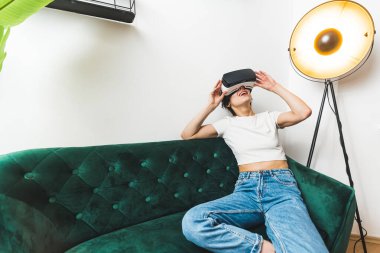  VR konsepti. Tam orta boy. Kanepesinde VR kulaklıkla oynayan biri. Yüksek kalite fotoğraf