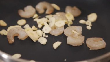 Şef tavada pişen karideslere ince dilimlenmiş sarımsak ekler ve karidesleri çevirmek için tavayı hareket ettirmeye başlar.